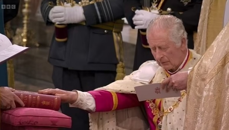 Rei Charles III lendo um cartão com suas falas durante juramento em coroação